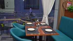 A restaurant with teal upholstered seating, wooden tables, and a fire extinguisher mounted on the wall. - Hotel Ramayana (Parbhani)