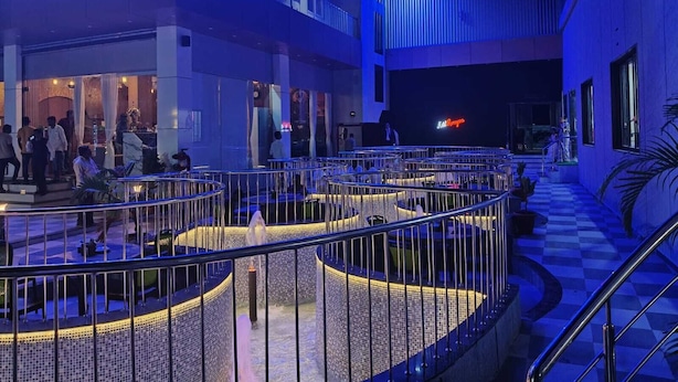 A spacious atrium with a checkered floor, a stage with a neon sign, and a seating area with a railing. - Hotel Ramayana (Parbhani)