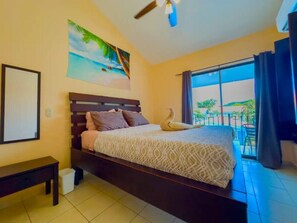 A bedroom with a bed, a bench, a painting, and a balcony with a view.