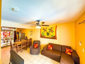 A living room with a ceiling fan, a dining area with chairs and a table, and a sofa with cushions.