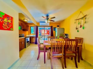 A dining area with wooden chairs and a table, a ceiling fan, and a view into a kitchen with cabinets and a refrigerator.