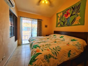 A bedroom with a bed, a window with curtains, a ceiling fan, and a painting on the wall.