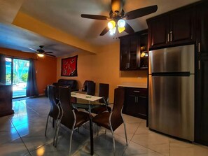 A modern kitchen with a dining table, chairs, a ceiling fan, and a stainless steel refrigerator.