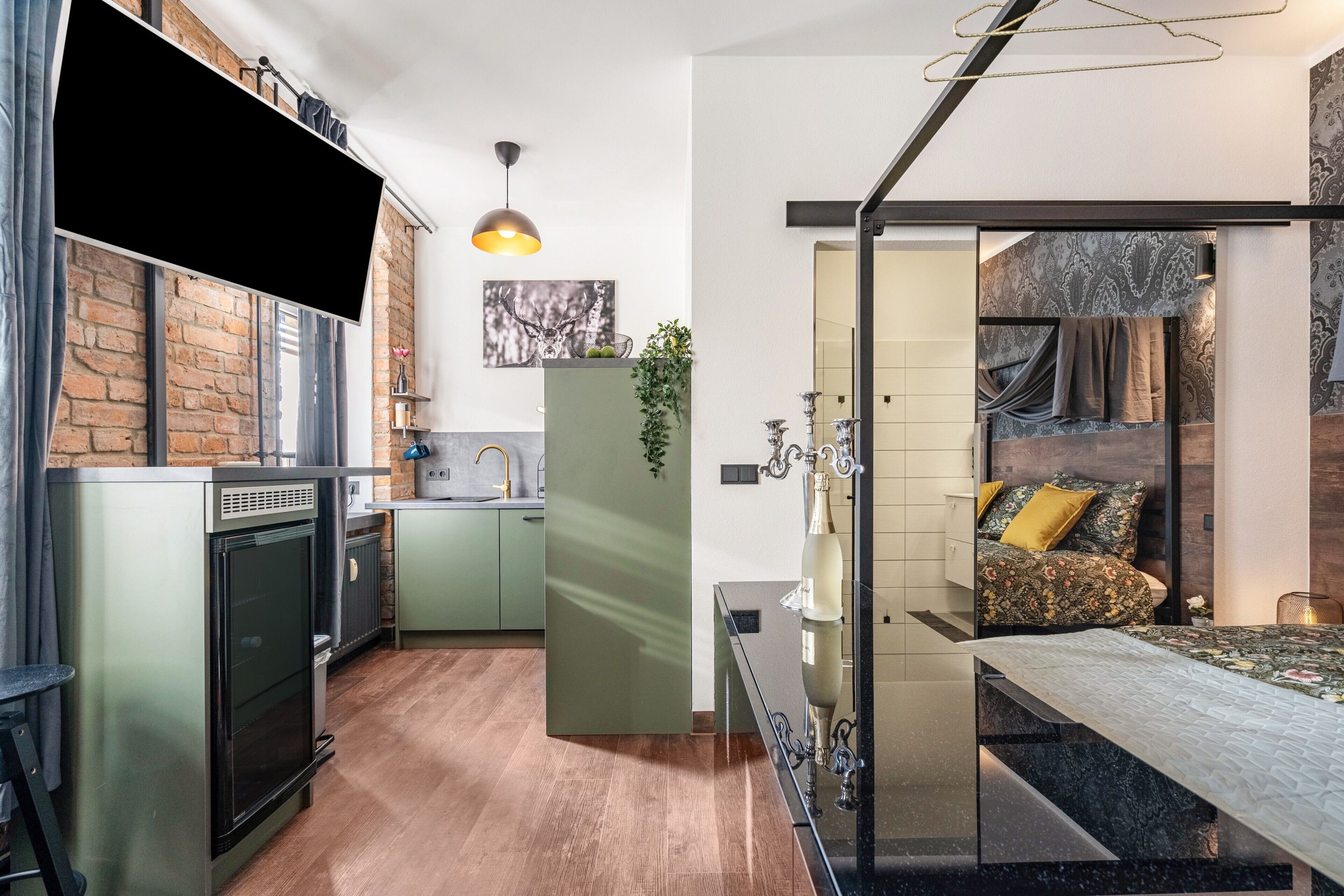 A compact kitchen with a built-in oven, a dining area with a glass partition, and a bedroom with a bed and a nightstand.