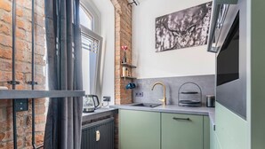 A compact kitchen with a brick wall, a window with curtains, a sink, and a stove. - Erz-Apartment Holiday Flat with Free Minibar and Wi-Fi (Jahnsdorf/Erzgeb)