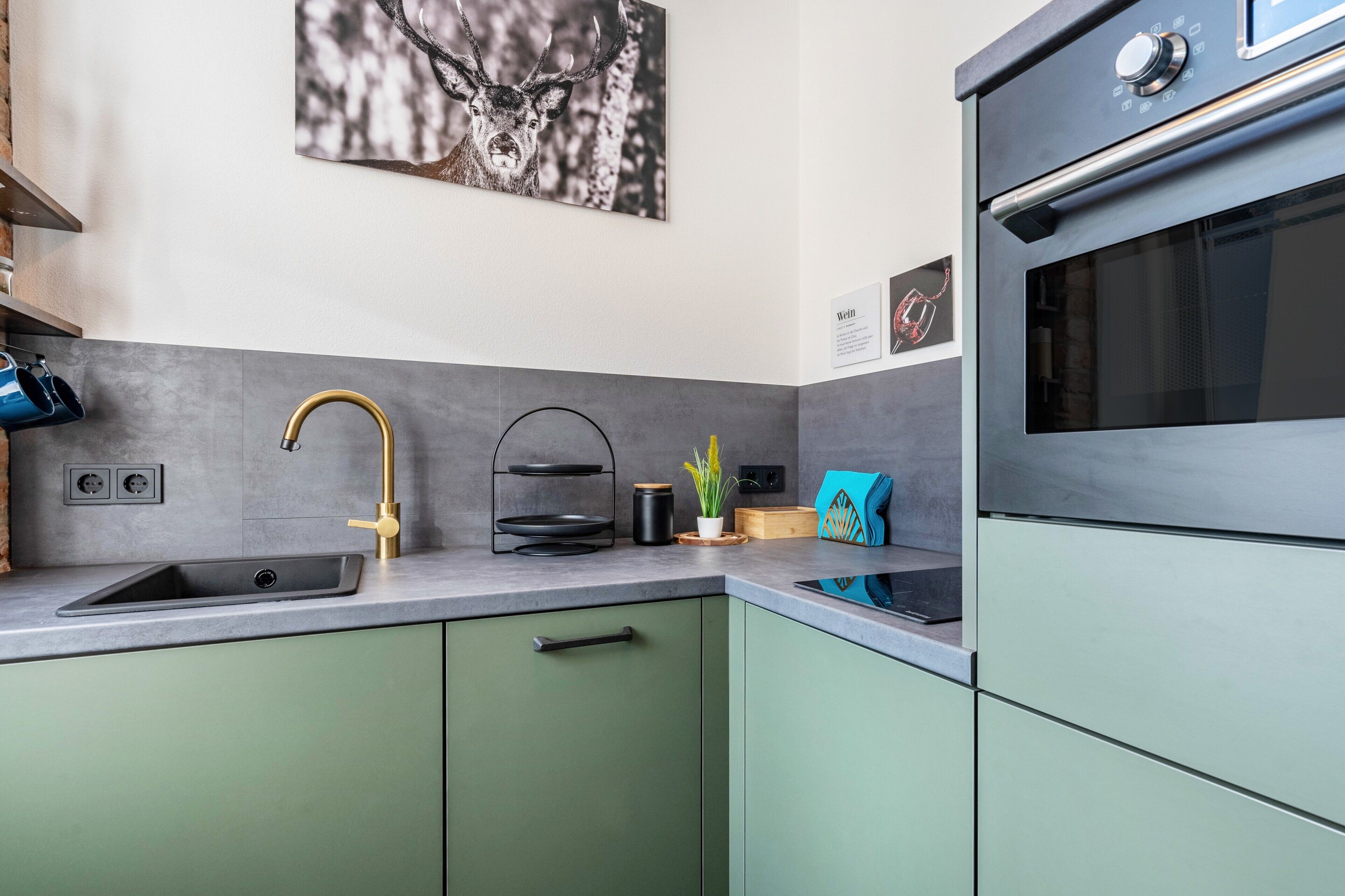 Eine Küche mit Spüle, Wasserhahn und Herd. An der Wand hängt ein gerahmtes Bild und auf der Arbeitsplatte steht eine Pflanze.