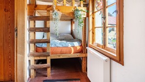 A wooden bunk bed room with a ladder, a window with a view, and hanging plants.