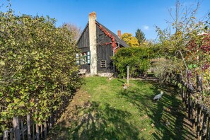 Une maison rustique avec un toit en pente, entourée d’un jardin délimité par une clôture en bois et agrémentée d’un petit arbre.