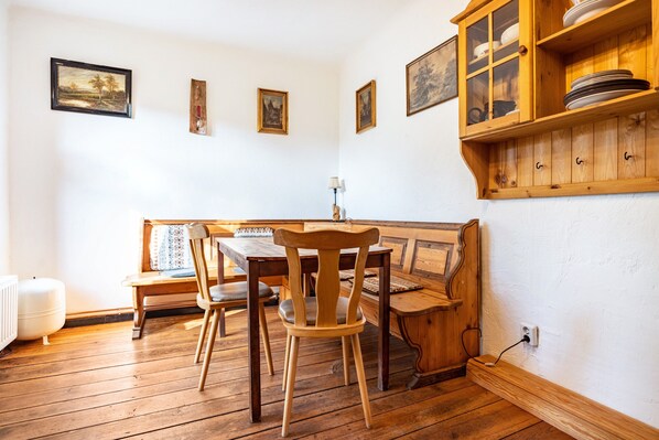 Une table à manger en bois, des chaises, un banc, un buffet rempli de vaisselle et des tableaux accrochés au mur.