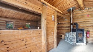 A wooden cabin interior with a stone fireplace, wooden walls, and a tiled floor.