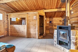 Interior de una cabaña de troncos con chimenea de piedra, paredes de madera y piso de baldosas.