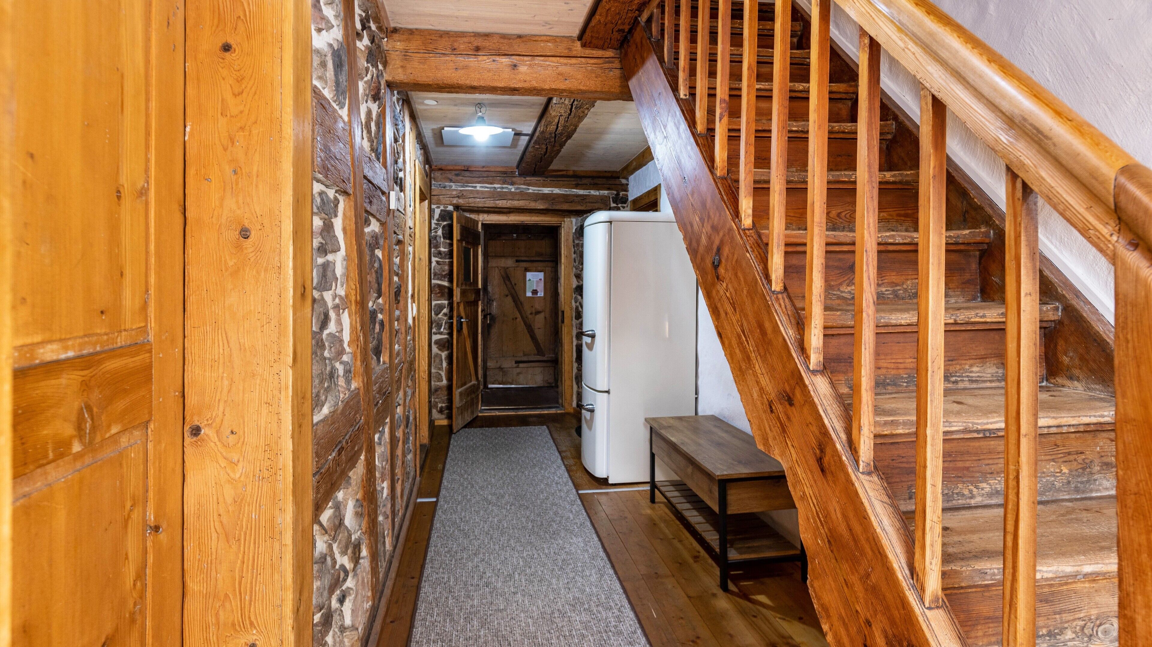 Un interno in legno con una scala, un frigorifero e una panca.