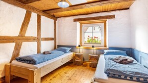 Una habitación con dos camas de madera, una ventana con vistas a flores y techo de madera.