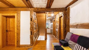 Un pasillo de madera con un sofá y una maleta, que conduce a una habitación con pared de piedra y ventana.