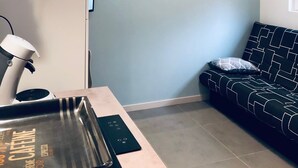 Eine moderne Küche mit einem weißen Kühlschrank, einer Kaffeemaschine und einer schwarzen Ablagefläche. An der Wand hängen zwei gerahmte Bilder und ein schwarz-weiß gemustertes Sofa.
