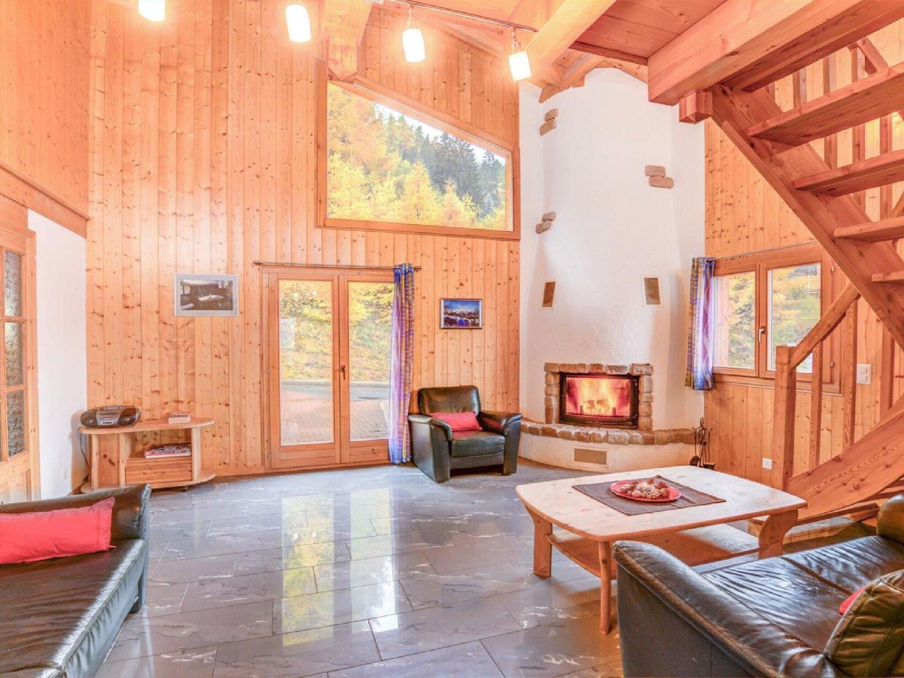 A spacious lodge room with a fireplace, leather seating, and a large window overlooking a forest.