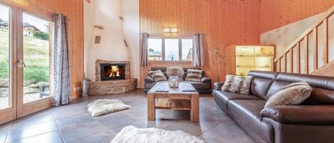 A spacious living room with a stone fireplace, leather sofas, and a large window offering a view of the outdoors.