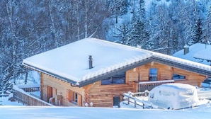 Una cabaña de madera con techo nevado, rodeada de un paisaje invernal y árboles.