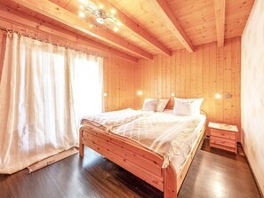 Ein Schlafzimmer aus Holz mit einem Bett, Vorhängen, einem Nachttisch und einer Deckenleuchte.