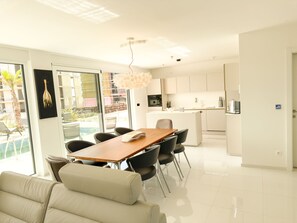 Relax in this spacious living area with a dining table, sofa, and kitchen, offering a view of the pool.