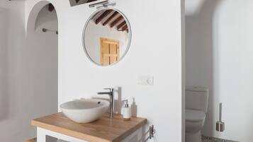Een badkamer met een houten wastafel, een ronde spiegel, een witte wasbak en een toilet.