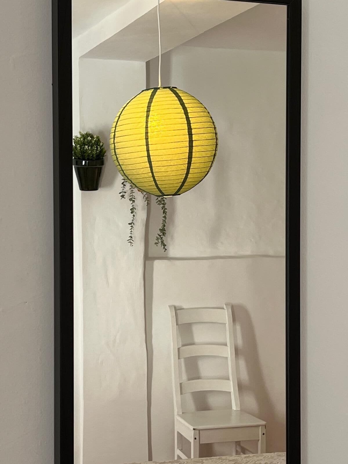 Una habitación con una silla blanca, un farol amarillo colgante y una pequeña planta en maceta.