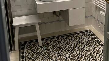 A bathroom with white subway tiles, a round mirror, a white sink, a small stool, and a patterned floor.