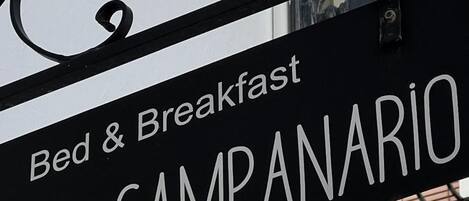 A sign for 'Bed & Breakfast Al Campanario' with a black metal lamp above it.