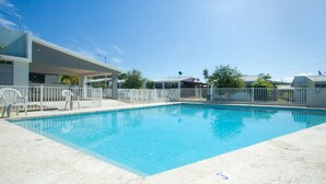 A rectangular swimming pool with a white deck and a covered area with chairs.