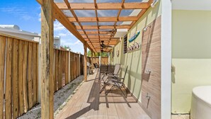 A covered outdoor patio with wooden flooring, a pergola, and a seating area with chairs.