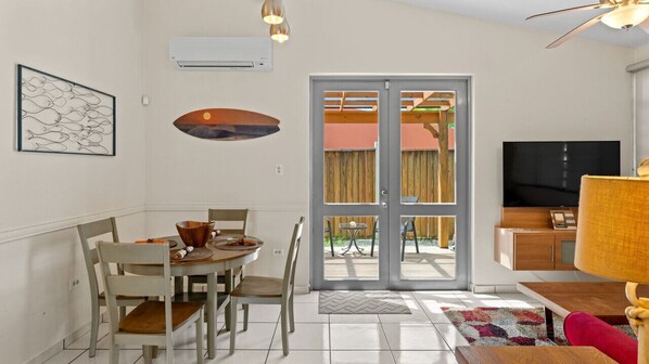 Un comedor con una mesa y sillas, un televisor y un puerta corrediza de vidrio que da a un espacio exterior.
