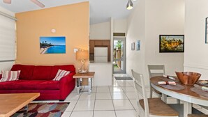 A modern living room with a red sofa, a wooden coffee table, and a dining area with a wooden table and chairs.