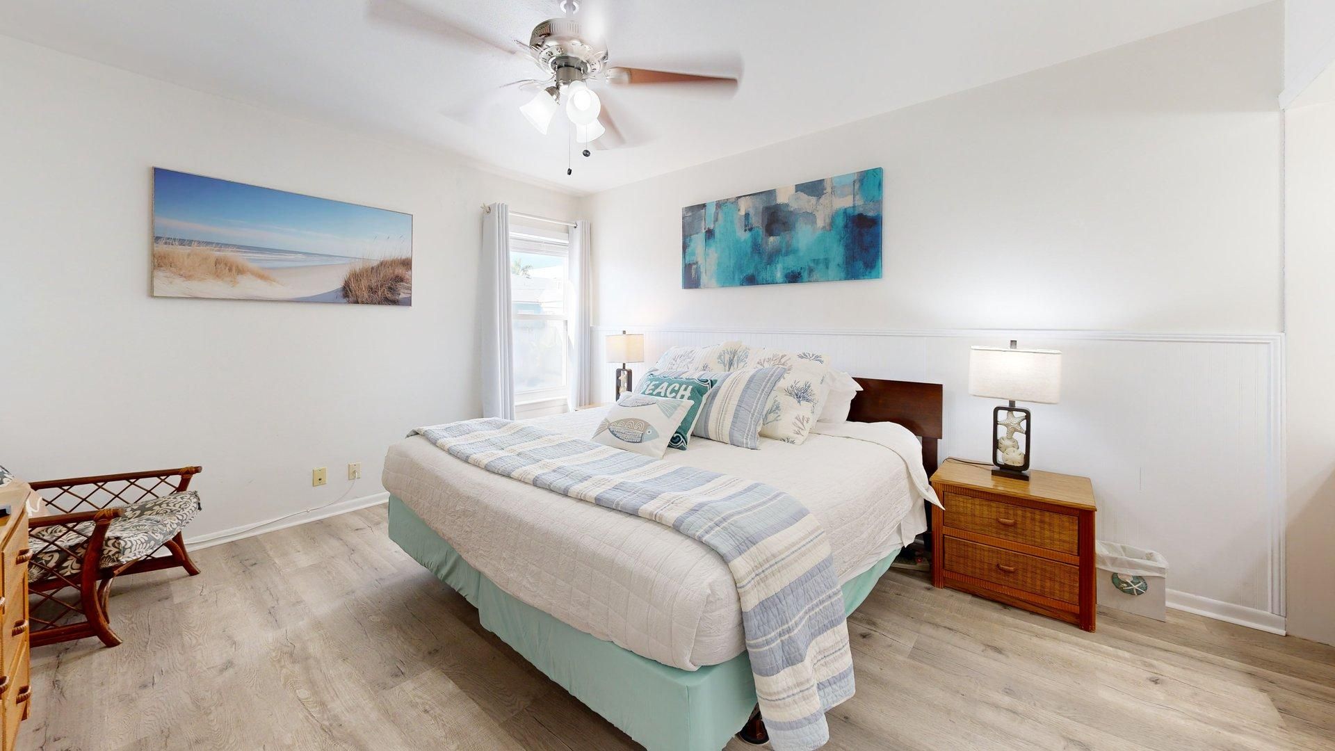 A bedroom with a bed, a nightstand, a chair, and artwork on the walls.