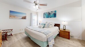 A bedroom with a bed, a nightstand, a chair, and artwork on the walls. - Beach Access Across the Street, Shared Heated Pool (Corpus Christi)