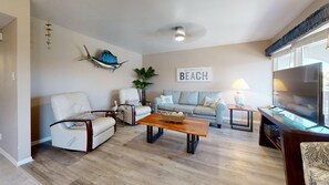 A living room with a sofa, chairs, a coffee table, a TV, and a wall with a 'BEACH' sign. - Beach Access Across the Street, Shared Heated Pool (Corpus Christi)
