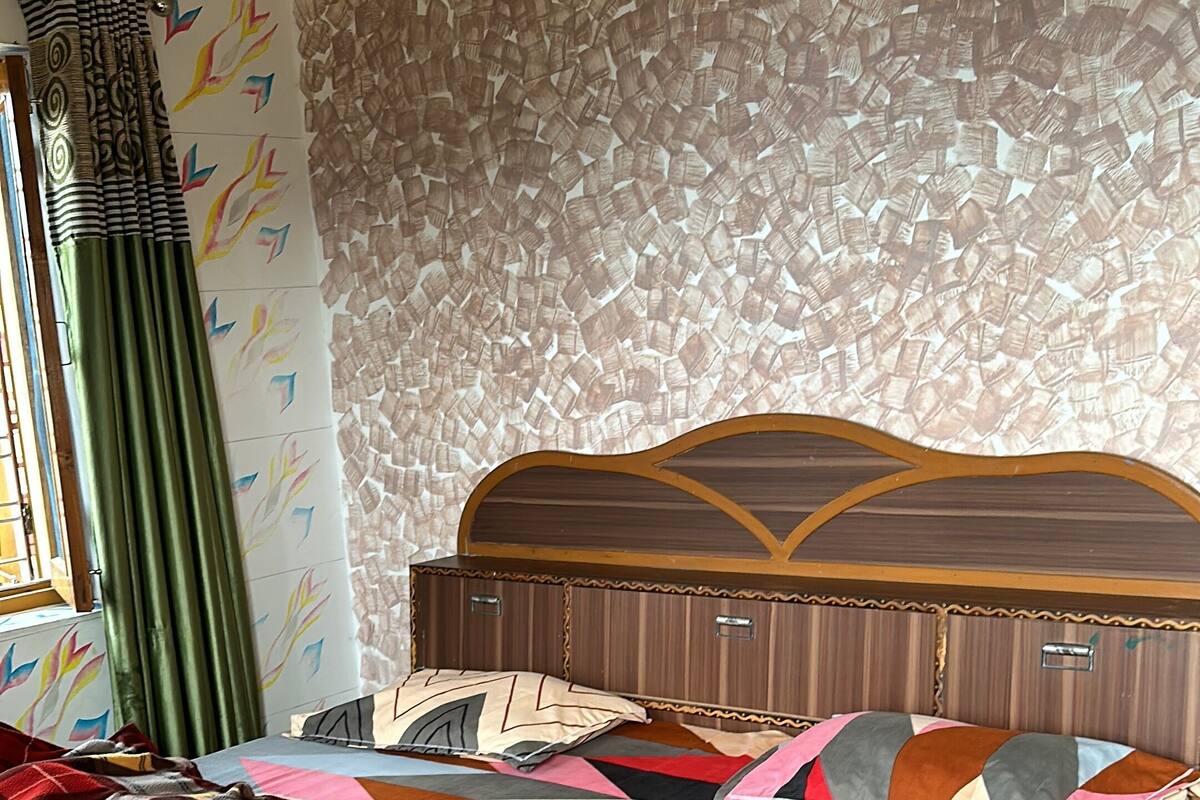 A bed with a patterned quilt, a headboard, and a wall with a geometric pattern.