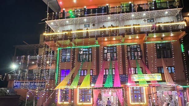 Un immeuble à plusieurs étages doté de balcons, de guirlandes lumineuses et d’une enseigne indiquant un espace de réception.