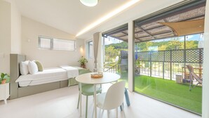 A modern room with a bed, a dining table with chairs, a balcony with a view of greenery and a fence. - Gyeongju Daol Dokchae Pension (Gyeongju)