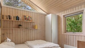 A bedroom with a bed, a wardrobe, a shelf with books and a painting, and a window with a view of trees. - "Tyyne" - 250m from the sea by Interhome (Sjællands Odde)