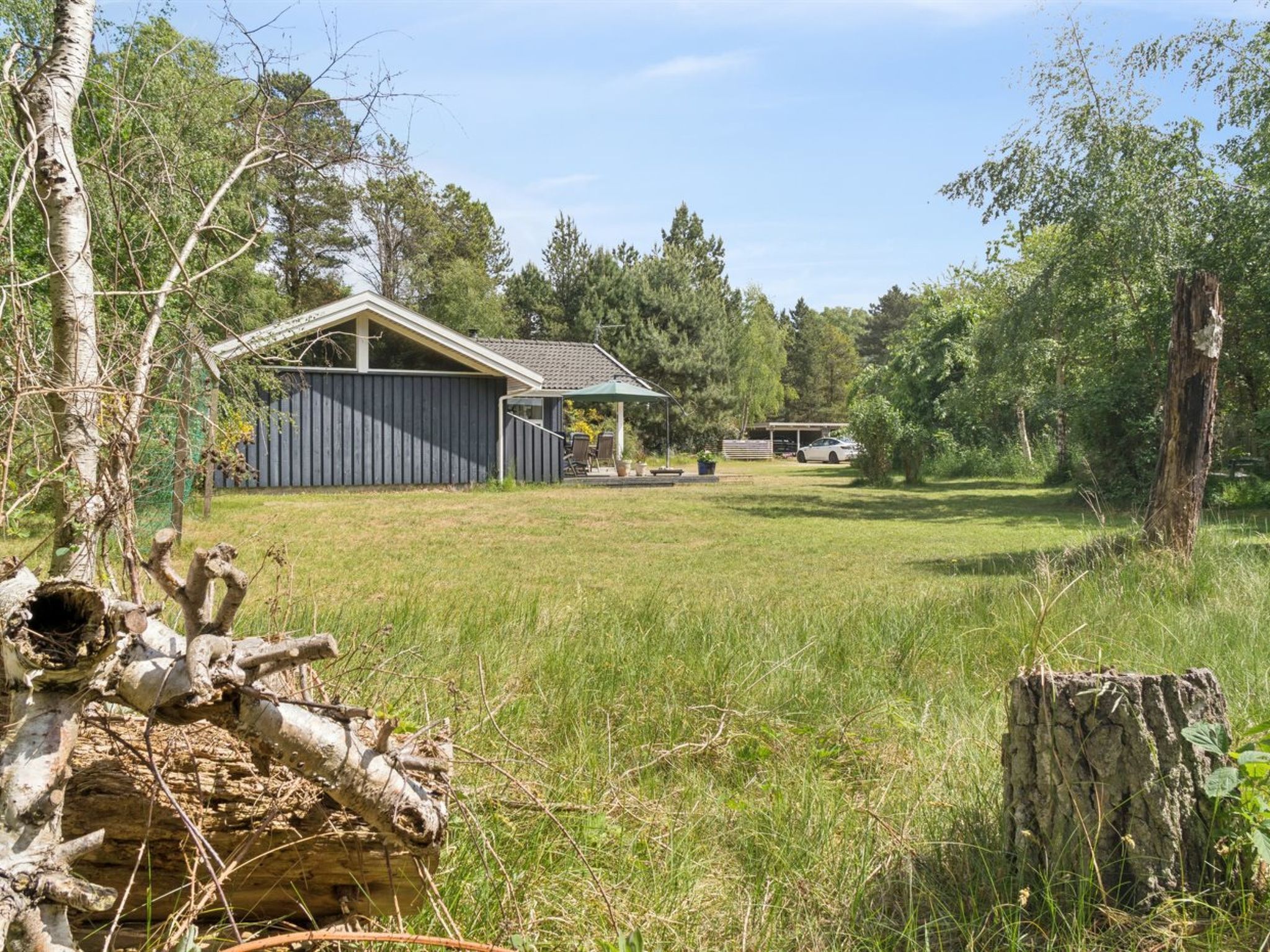 Une propriété rurale avec un chalet en bois, un espace de détente extérieur abrité et une voiture garée à l’arrière-plan.