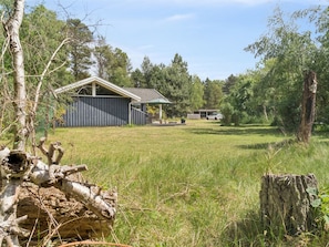 A rural property with a wooden cabin, a covered outdoor seating area, and a car parked in the background.