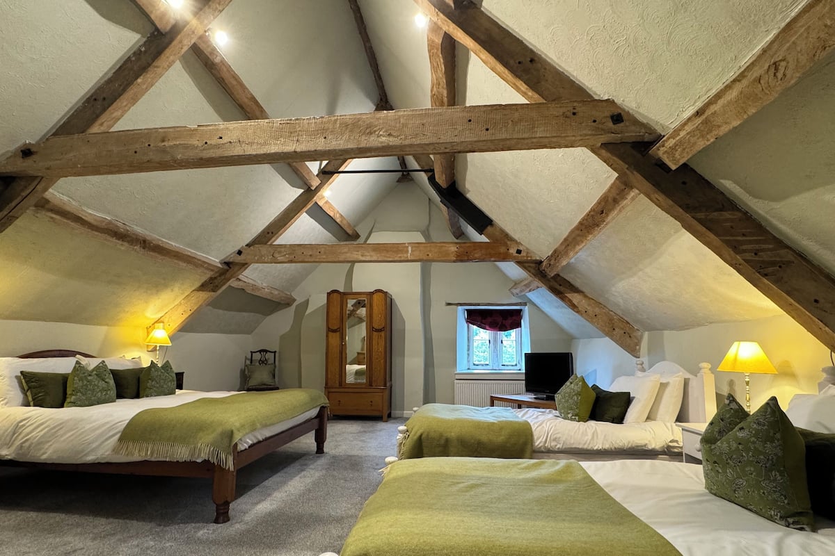 Un dormitorio acogedor en el ático con dos camas, vigas de madera, un espejo grande y una ventana con vistas.