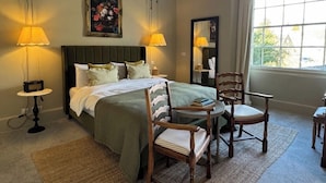 A hotel room with a large bed, two bedside lamps, a mirror, a window with a view, and a small table with chairs. - The Neeld Arms (Chippenham)
