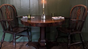 A round wooden table with two chairs, a lit candle, salt and pepper shakers, and a green wall with a wall-mounted light fixture. - The Neeld Arms (Chippenham)