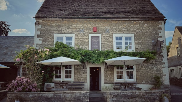 A stone building with a traditional design, featuring a pub sign and outdoor seating with umbrellas. - The Neeld Arms (Chippenham)