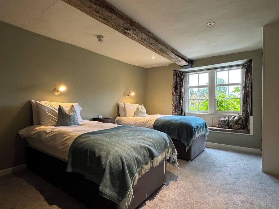 A bedroom with two beds, a window with curtains, and a ceiling with exposed beams.