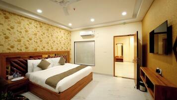 A hotel room with a large bed, a ceiling fan, an air conditioning unit, a TV, and a wooden nightstand.