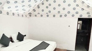 Een slaapkamer met een bed, kussens, een nachtkastje en een deur naar de badkamer.