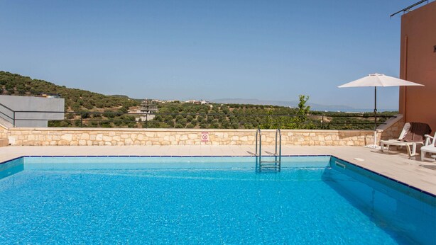 Una piscina azul cristalina con un muro de piedra y vistas a las colinas al fondo.