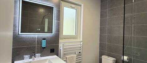 Un baño moderno con lavamanos blanco, espejo, inodoro y cabina de ducha de vidrio.